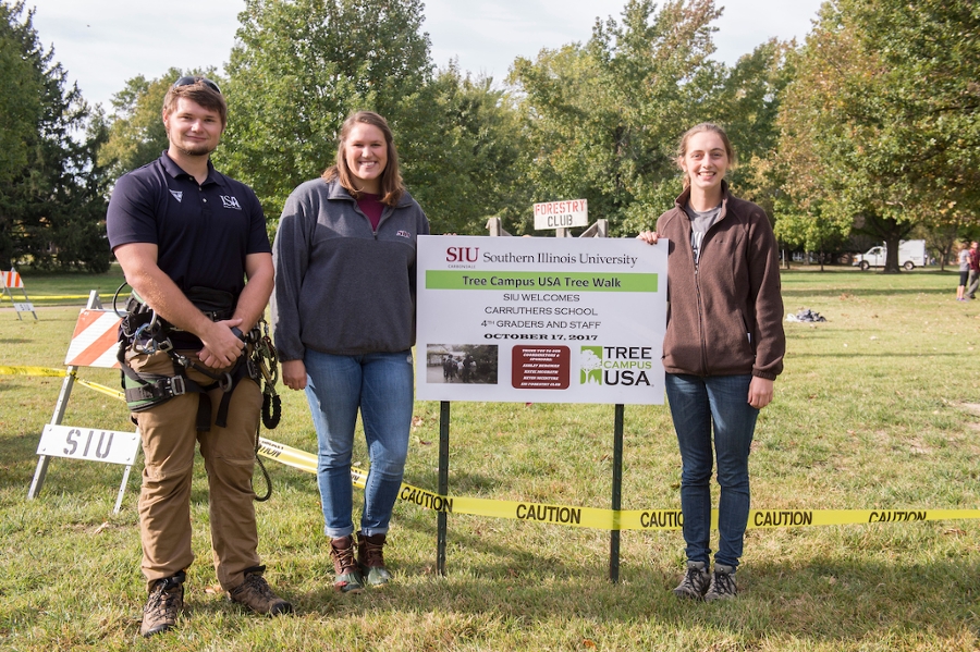 three people in front of a SIU tree campus USA sign