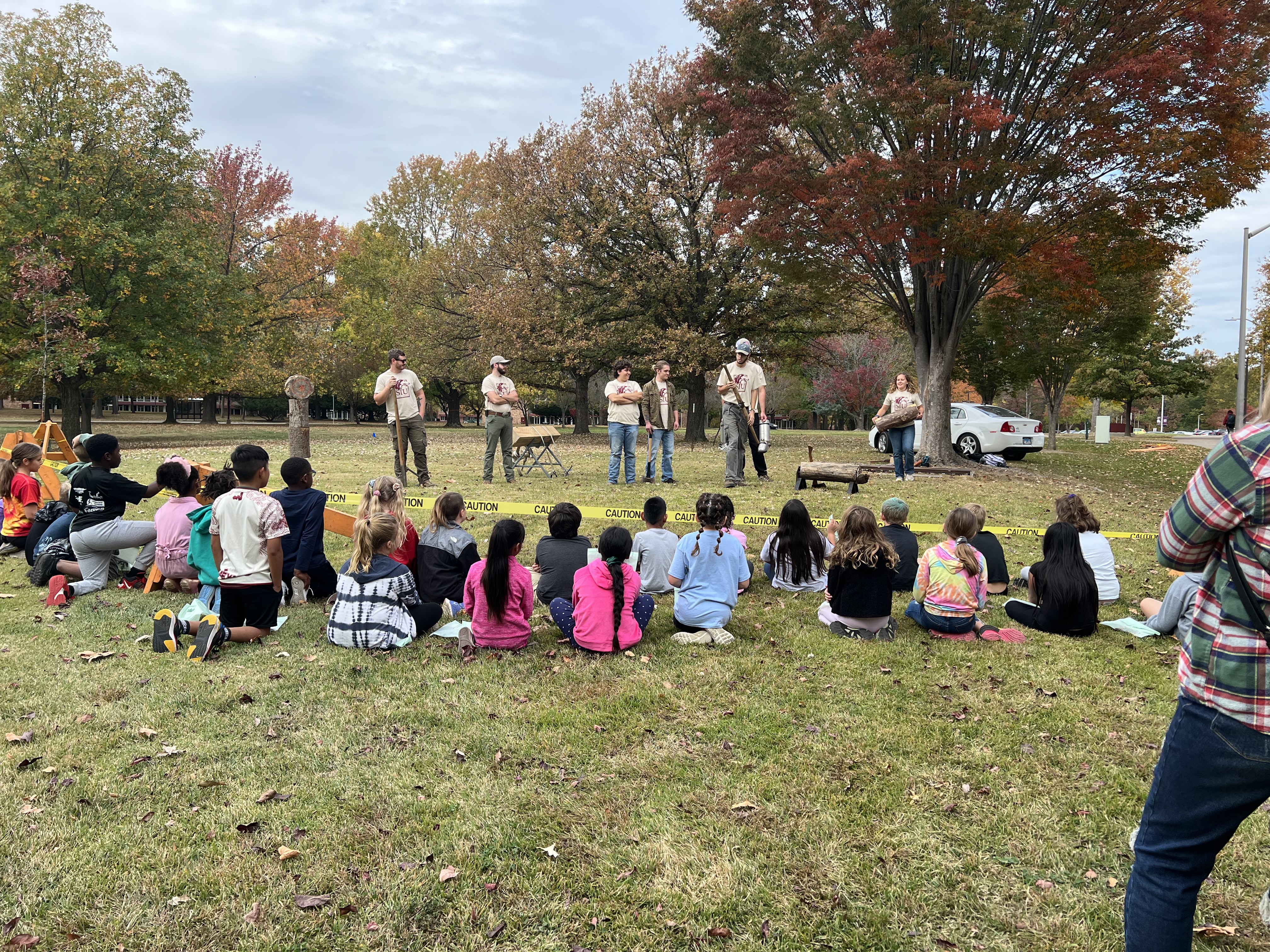 group of kids sitting down to watch a demonstration outside